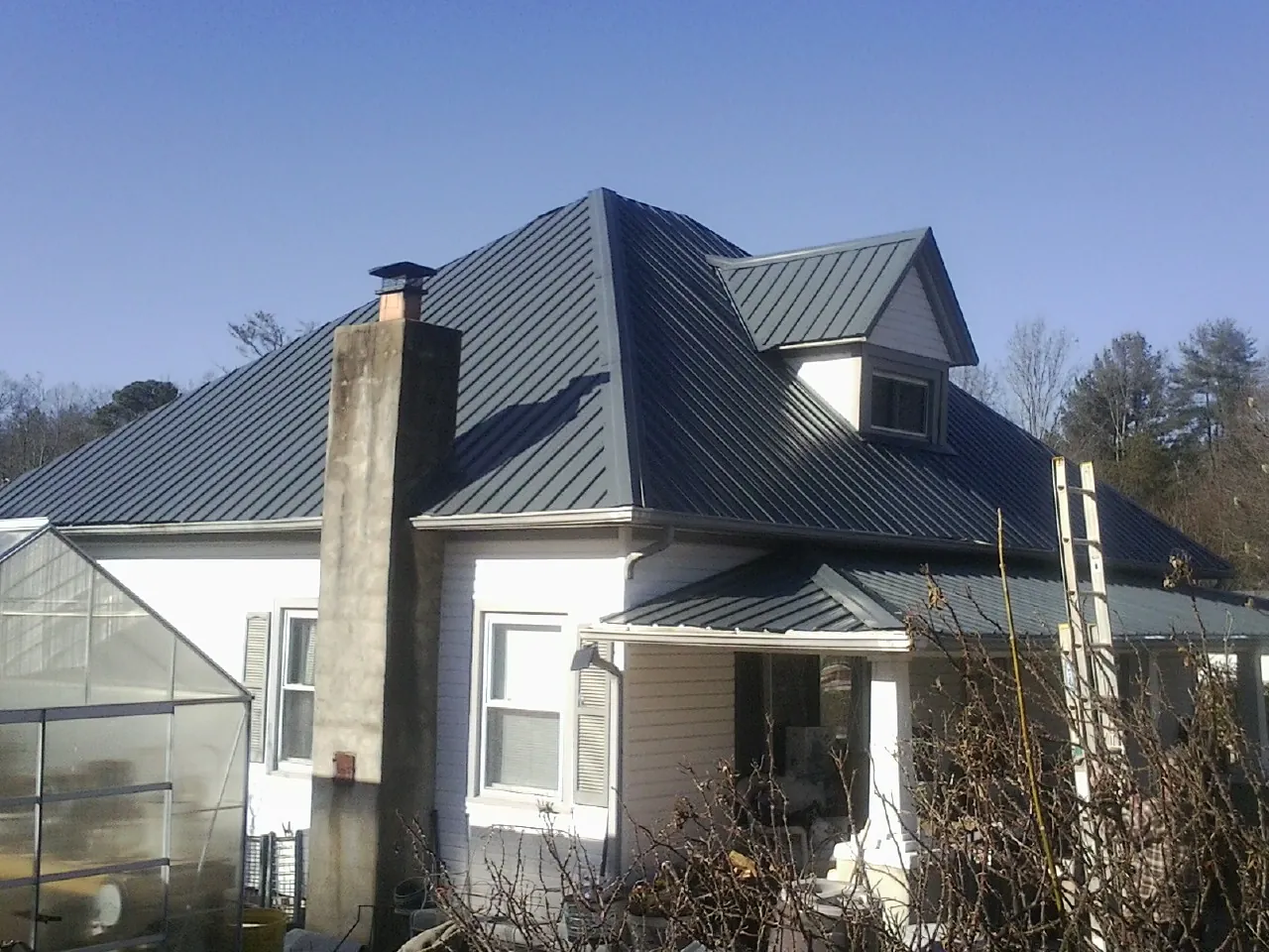 Dark blue standing seam metal roof on a white farmhouse with dormer — Slate & Tile Roof Repair by Roofing Brothers in Parkhill