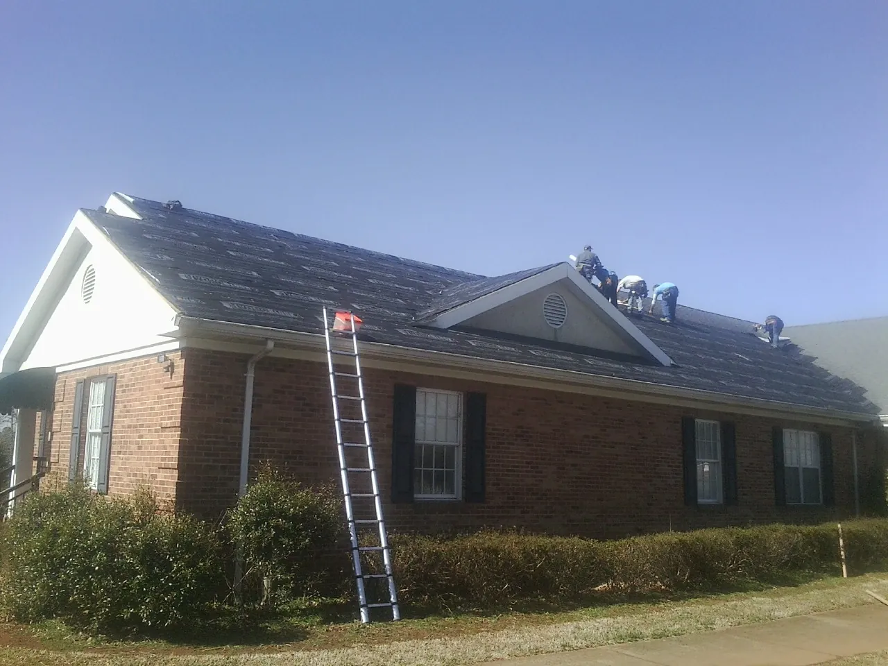 Crew tearing shingles off a brick ranch roof with a ladder set — Metal Roof Repair work by our crew in Parkhill