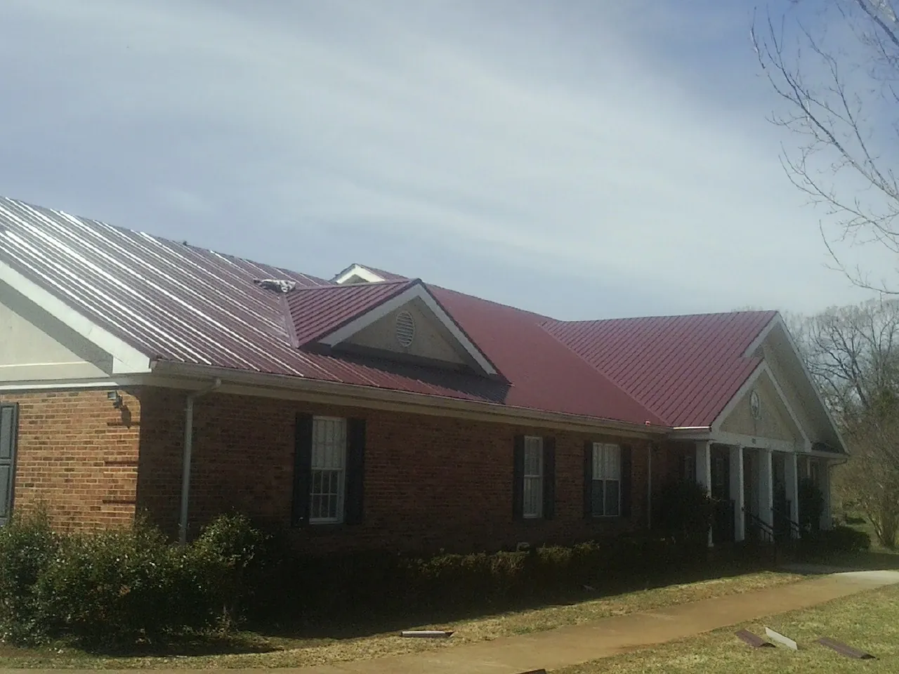 Red metal roof with gabled entries on a long brick building, from a Hail Damage Roof Repair job in Parkhill