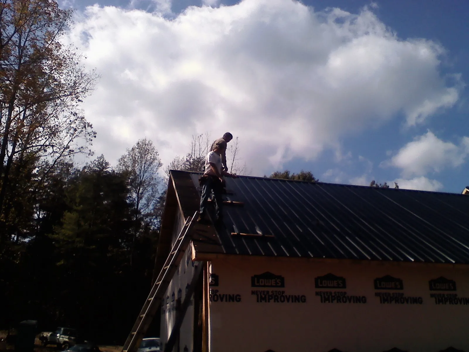 Roofer fastening dark metal panels high against a cloudy sky, from a Roof Inspection job in Parkhill