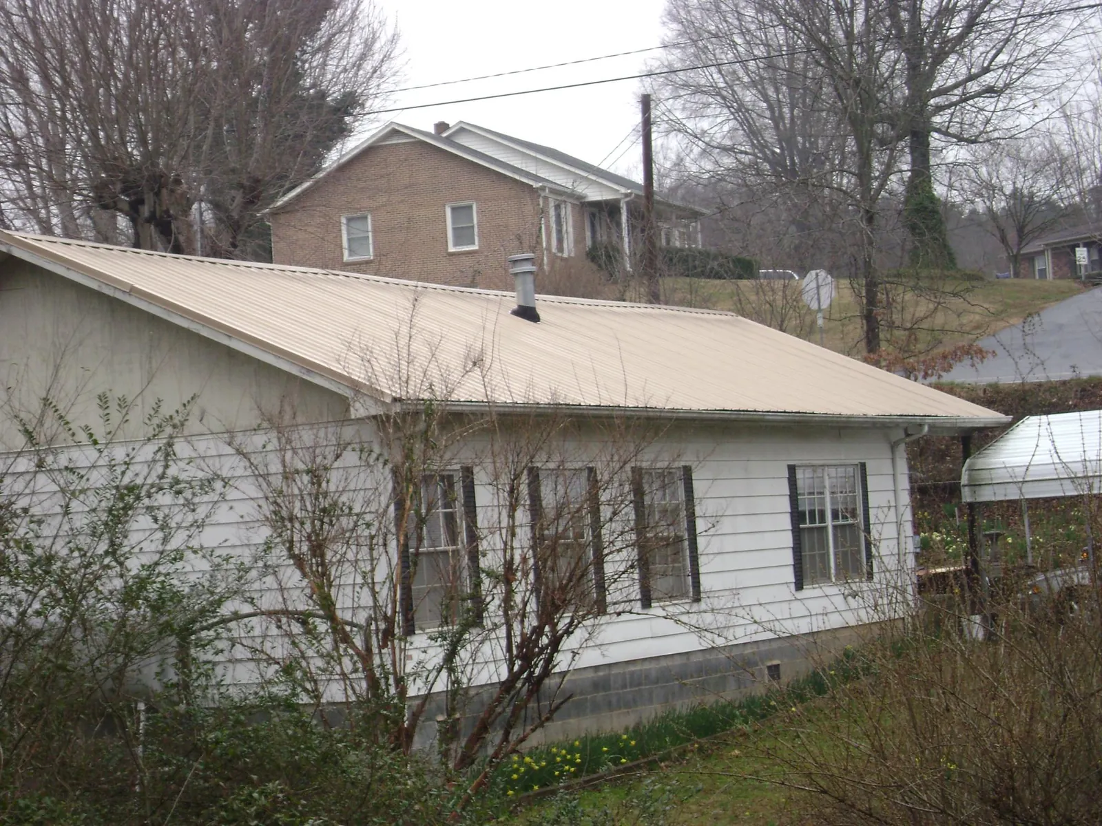 Tan metal roof on a white sided house set into a hillside — Commercial Roofing by Roofing Brothers in Parkhill
