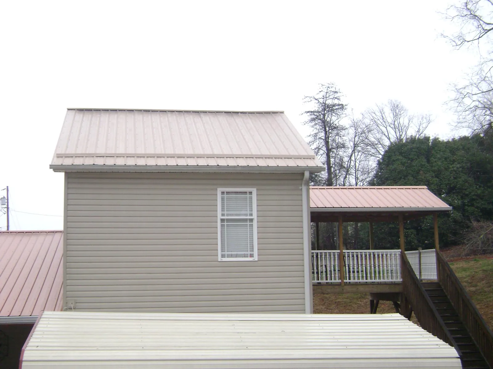 Tan metal roofs on a two story addition and attached porch, from a Roof Replacement job in Parkhill